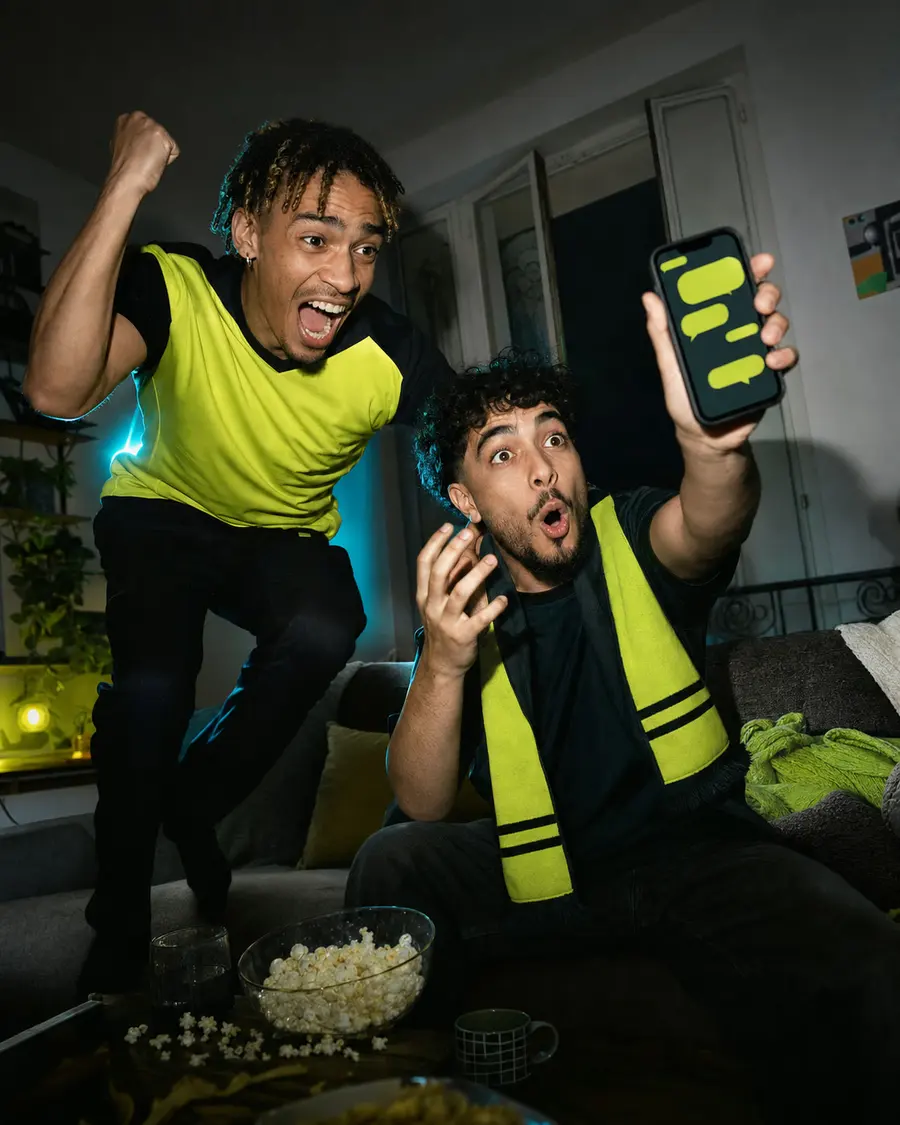 Deux amis explosent de joie devant un match, téléphone en main avec le tchat wazap